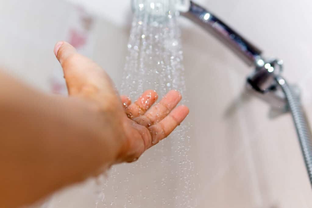 male and under the stream of water from the shower, checks the water temperature selective focus