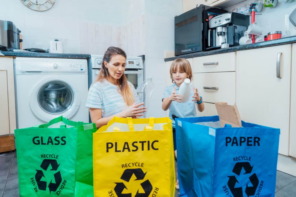 Mother is teaching kid how to recycle help the boy aware environmental importance - mom educates son sort garbage into different bins on kitchen. Family sorting garbage at home. Concept of recycling